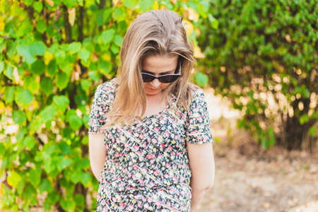 Shy girl standing and looking down - Ashamed woman holding hands behind her back - Nervous teen with sunglassesの写真素材
