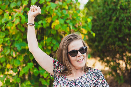 Winner girl holding fist up in the air - Happy successful woman or student wearing sunglasses while being excitedの写真素材