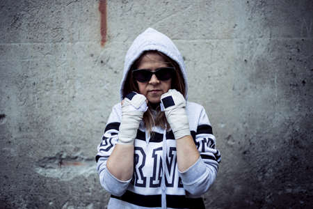 Woman fighter in guard position - Ghetto girl wearing sunglasses ready to fight having a grunge wall behind as backgroundの写真素材