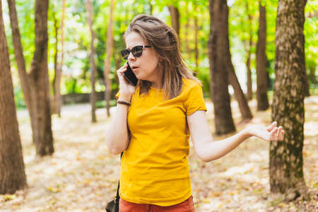 Beautiful young woman talking on the mobile phone in the park - Angry teen girl wearing sunglasses receiving an unknown call - Surprised sad female holding a telephone while walking outsideの写真素材