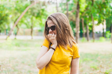 Nervous woman biting nails - Anxious girl with sunglasses and yellow t shirt having an addiction of nibbling fingernailの写真素材