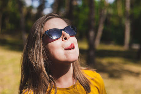Pretty girl sticking out tongue - Funny and playful woman grimacing in the sunlight in the forest enjoying summerの写真素材
