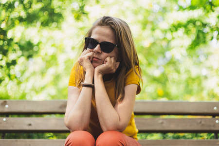 Pensive woman thinking about the future - Sad lonely girl sitting on a bench while daydreaming or being exhaustedの写真素材