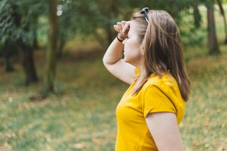 Lost young woman looking in the distance for directions â Girl with brown hair wearing sunglasses holding hand over her forehead on a hot summer dayの写真素材