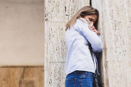 Woman is hiding scared behind a wall - Girl having a panic attack and embracing herself at the...