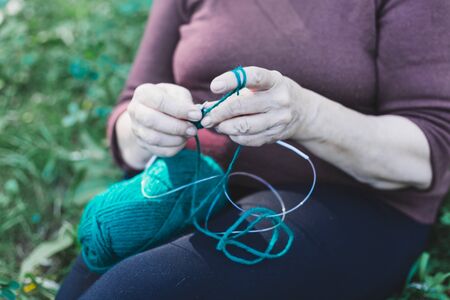 Close-up of senior woman knitting outside while sitting on the grass - Fun and relaxing activity for all ages - Elderly person making clothesの写真素材