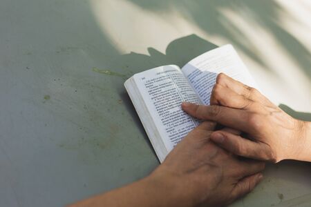 Young woman reading from small Bible outside in a park on a summer day â Top view girl lecturing from Holy Book while following words with her fingerの写真素材