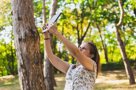 Woman taking photo with a tablet outside - Girl in her twenties taking some pictures or filming in a forest - Nature documentaryの写真素材