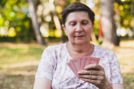 Senior playing cards outdoors - Old woman having fun outside and enjoying her positive retirement...