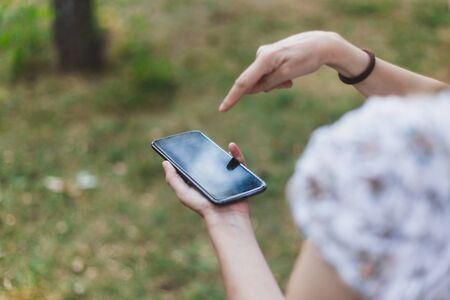 Young person holding and tapping the screen of a mobile phone outdoors - Using black modern gadget with touch screen for textingの写真素材
