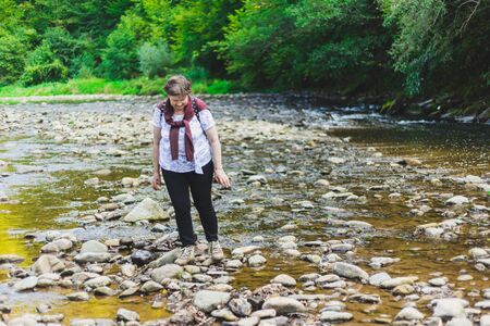 Happy senior woman walking alone in nature near a river on a summer day â Pretty old lady relaxing and feeling good outsideの写真素材