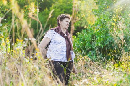 Relaxed senior woman walking alone in nature on a summer day - Casually dressed cute old lady enjoying peaceful and serene time in the wildernessの写真素材