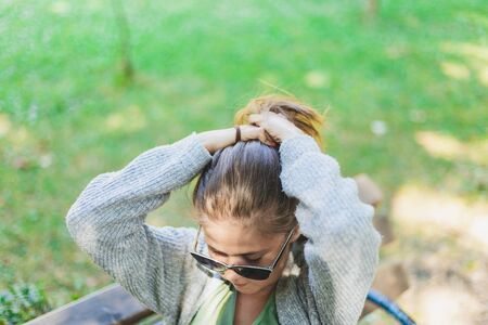 Woman tying hair upside - Girl fixing her look outside sitting on a bench - Teenager dying her own hairstyle modelの写真素材