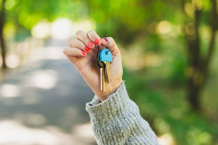 Woman hand holding keys up in the air - Concept of selling, buying or renting a real estate as female agentの写真素材