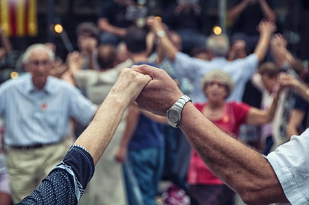 View of senior people holding hands and dancing national dance Sardana at Plaza Nova, Barcelona, Spain. It is a type of circle dance typical of Cataloniaの写真素材