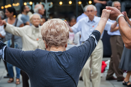 View of senior people holding hands and dancing national dance Sardana at Plaza Nova, Barcelona, Spain. It is a type of circle dance typical of Cataloniaの写真素材