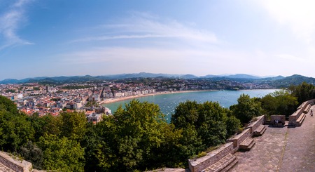Aerial view of popular touristic city San Sebastian, Basque Country, Spain with beach, old buildings, fort, trees and mountains at the background. Cloudy blue skyの写真素材