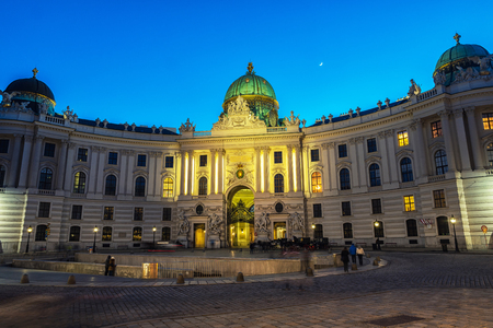 Vienna, Austria. Illuminated Hofburg Palace seen from Michaelerplatz at night. Motion blurred people, clear sky with moon. Popular landmark in the cityのeditorial素材