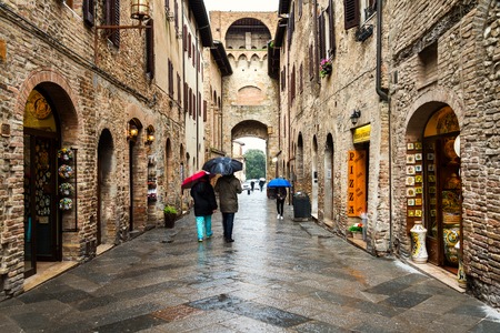 SAN GIMIGNANO, ITALY - MARCH 6, 2016: Unidentified people holding umbrellas and walking by the streets of old town in Sienaのeditorial素材