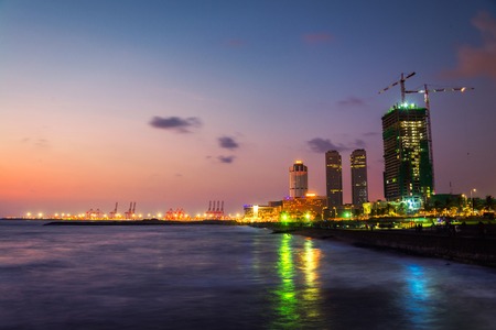 Cityscape of Colombo, Sri Lanka with modern buildings at night. Ocean waves at night and sunset cloudy sky. People at promenade areaの写真素材