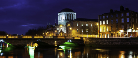 Illuminated Four Courts building in Dublin, Ireland at night. Reflection in Liffey river with bridge, various cafes, shops and restaurantsの写真素材