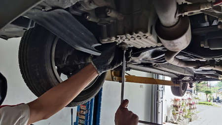 An Indonesian car mechanic is replacing an oil filter under the car in an authorized workshop dealershipの写真素材