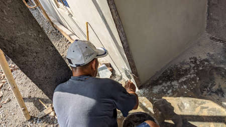 An old male Indonesian builder is plastering a wall edge using traditional toolsの写真素材