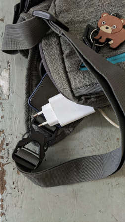 a smartphone and its charger come out of a gray bag with a cute keychain in the shape of a bear
