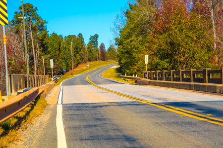 A road and bridge in the country with Fall colors and blue skies scene