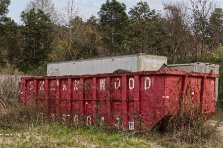 Augusta, Ga USA - 03 17 21: Urban scene a red open top dumpster overgrown foliageのeditorial素材