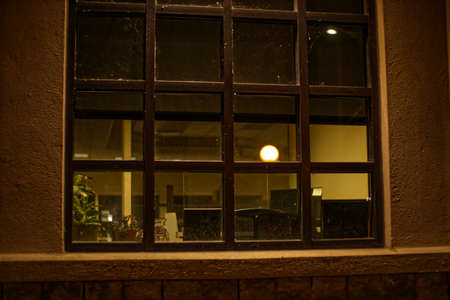 A dirty office building window at night with lamp post reflections