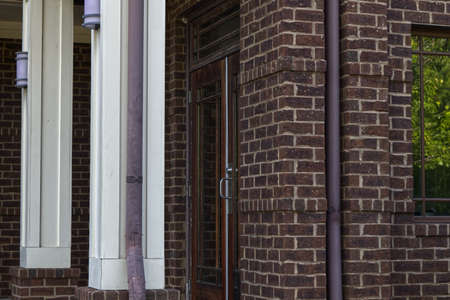 Close up vintage style brick facade Door with silver handle brown gutters and beautiful green...