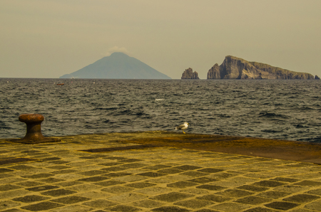 Island of panarea pier seagull and on the horizon stromboli island with its volcano and several cliffs in the tyrrhenian seaの写真素材
