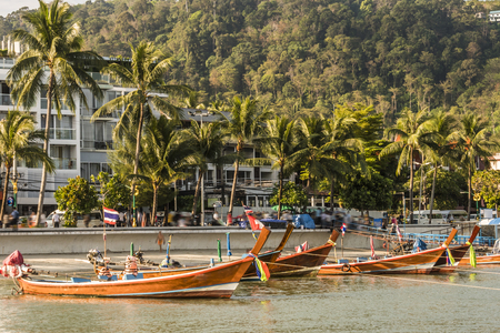 typical boats of the area on the island of Phuket back you can see a small beach and buildings near the port Thailandの写真素材