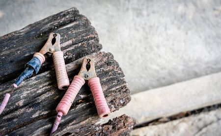 Old dirty rusty jumper cable for charging a car battery on a wooden table with a concrete...