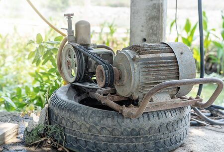 Old electric motor pumping machine on a black car wheel using for farming or gardening in the house with green background at summer sunrise. The idea for technology and facilities in agriculture.の写真素材
