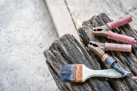 Old dirty rusty paintbrush and jumper cable for charging a car battery on a wooden table with a concrete background and a copy space to put text on the left. Vintage style photo and abstract concept.の写真素材