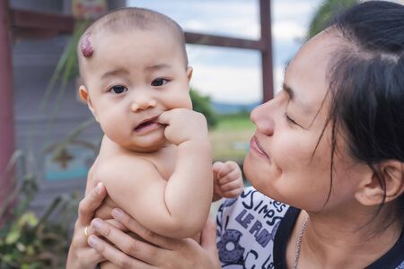 Portrait photo of an adorable little baby girl is sucking and biting her thumb fingers thoughtfully, playing with her family happily. Baby development of 5-6 months aged and oral healthcare concept.の写真素材