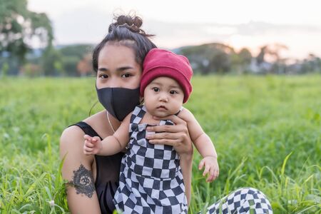 Portrait of a happy Asian mother wears black mask and plays with her young daughter in the summer...