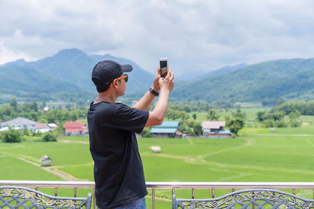 Nan, Thailand-October 18, 2020:  An unidentified man using a smartphone for taking photos view of the landscape in green rice plantation mountain background in Nan province, northern Thailandのeditorial素材