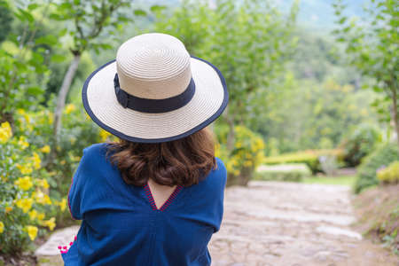 Back view of Adult woman in summer day wearing a straw hat and blue native clothes relaxing and looking top view on stairs of the walkway down the garden in the vacation morning with nature backgroundの写真素材