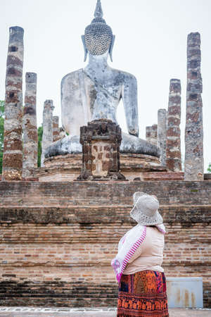 Adult woman looking at back view of Ancient Buddha image with the ruins of temple at Sukhotai Historical Park, UNESCO world heritage and Famous Tourist Destination in Northern Thailandのeditorial素材