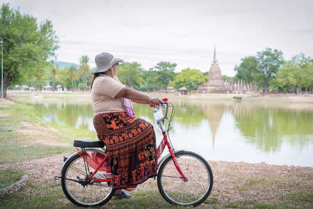 Sukhothai, Thailand-October 20, 2020:  An unidentified woman riding a bicycle looking at the old Buddhist temple  at Sukhotai Historical Park,  Famous Tourist Destination in Northern Thailandのeditorial素材