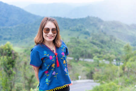 Adult traveling woman wearing sunglasses standing and smiling on the top of the mountain cliff with...