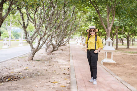 Beautiful adult Asian woman wearing a straw hat and sunglasses relaxing and smiling on the pathway...