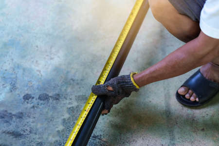 Close up of man's hands holding the tape measure and steel for measuring work part in a workshop,...