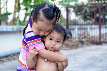 Close-up of adorable little child girl looking at camera while elder sister embracing beloved little kid outdoor, enjoying time together at home, happy family having fun playing cuddling and hugging.の写真素材