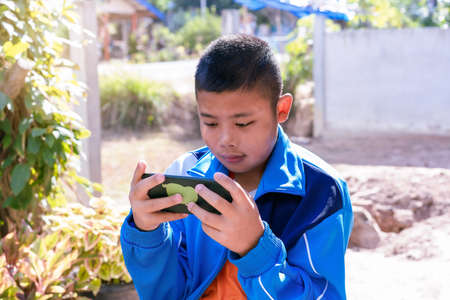 Portrait of child boy playing online games with smartphone, sitting outdoor play with phone in hand...