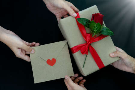Two Women hands changing presents and celebrating holidays together. Romantic couple giving gift box and a red rose, letter with red heart, as handmade gifts for Valentine's Day or other days holidayの写真素材