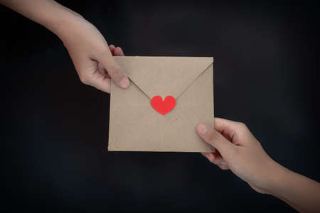 Close-up of Women giving card letter with red heart on the table, black background. Concept of creating handmade gifts for Valentine's Day or other days holidayの写真素材